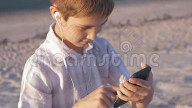 一个男孩在海滩上玩智能手机。 10岁的孩子喜欢坐在沙滩上的智能手机